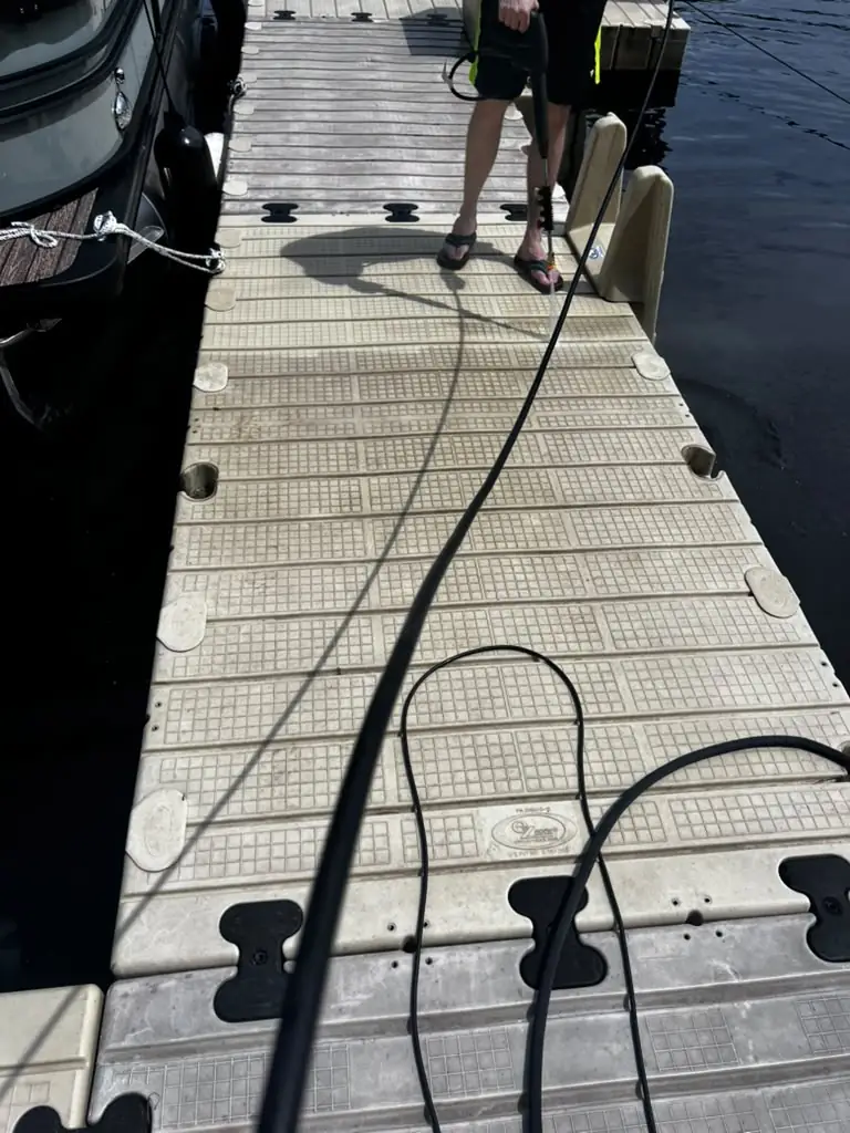 NSA Cleaning technician power washing a floating boat dock beside a moored pontoon boat