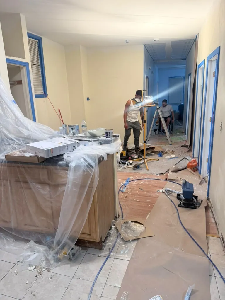 Painting crew prepping an apartment with plastic sheeting and blue tape