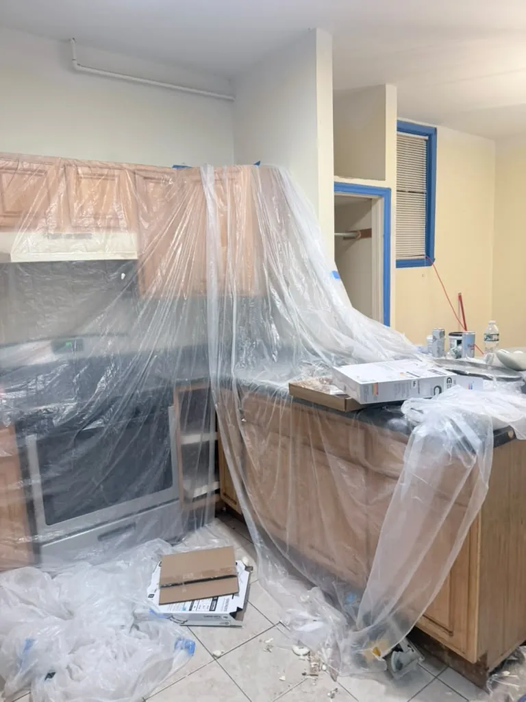 Kitchen cabinets and appliances masked with plastic sheeting before interior painting and post-construction cleaning