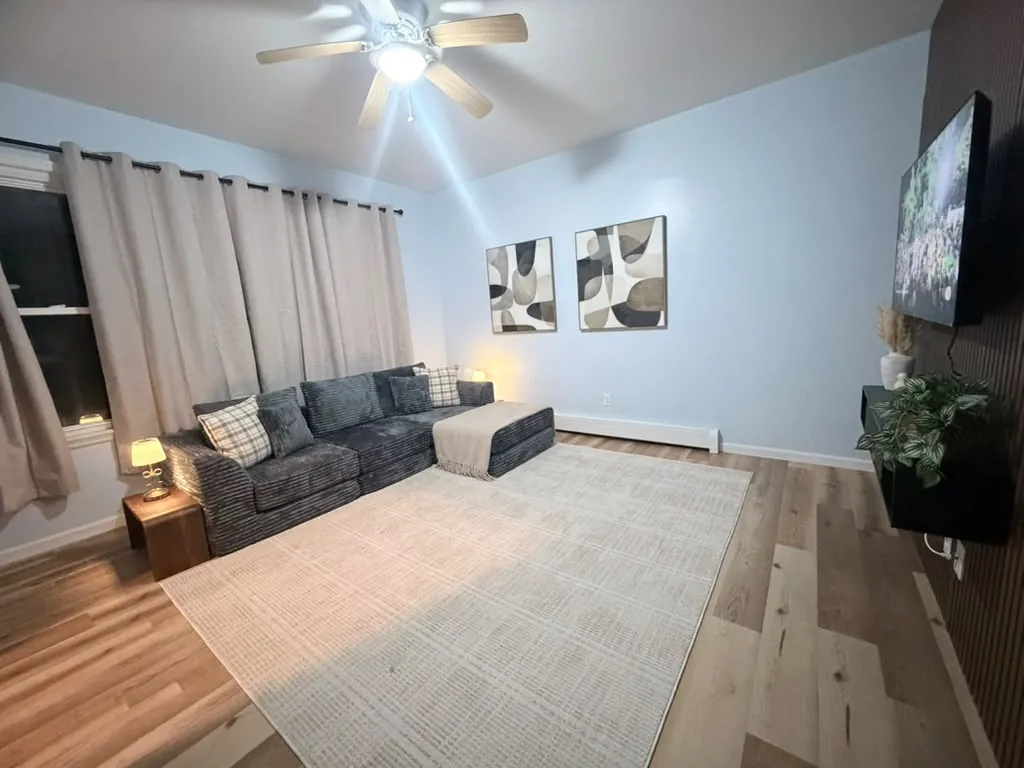 Clean living room with gray sectional, area rug and ceiling fan after a residential cleaning